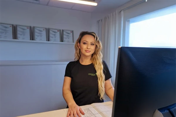 Kvinna med långt hår står vid skrivbordet framför en dator.