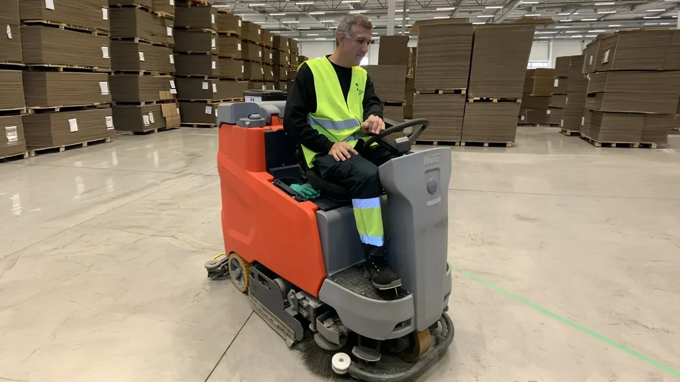 En person kör en skrubbare i ett lager med lådor.