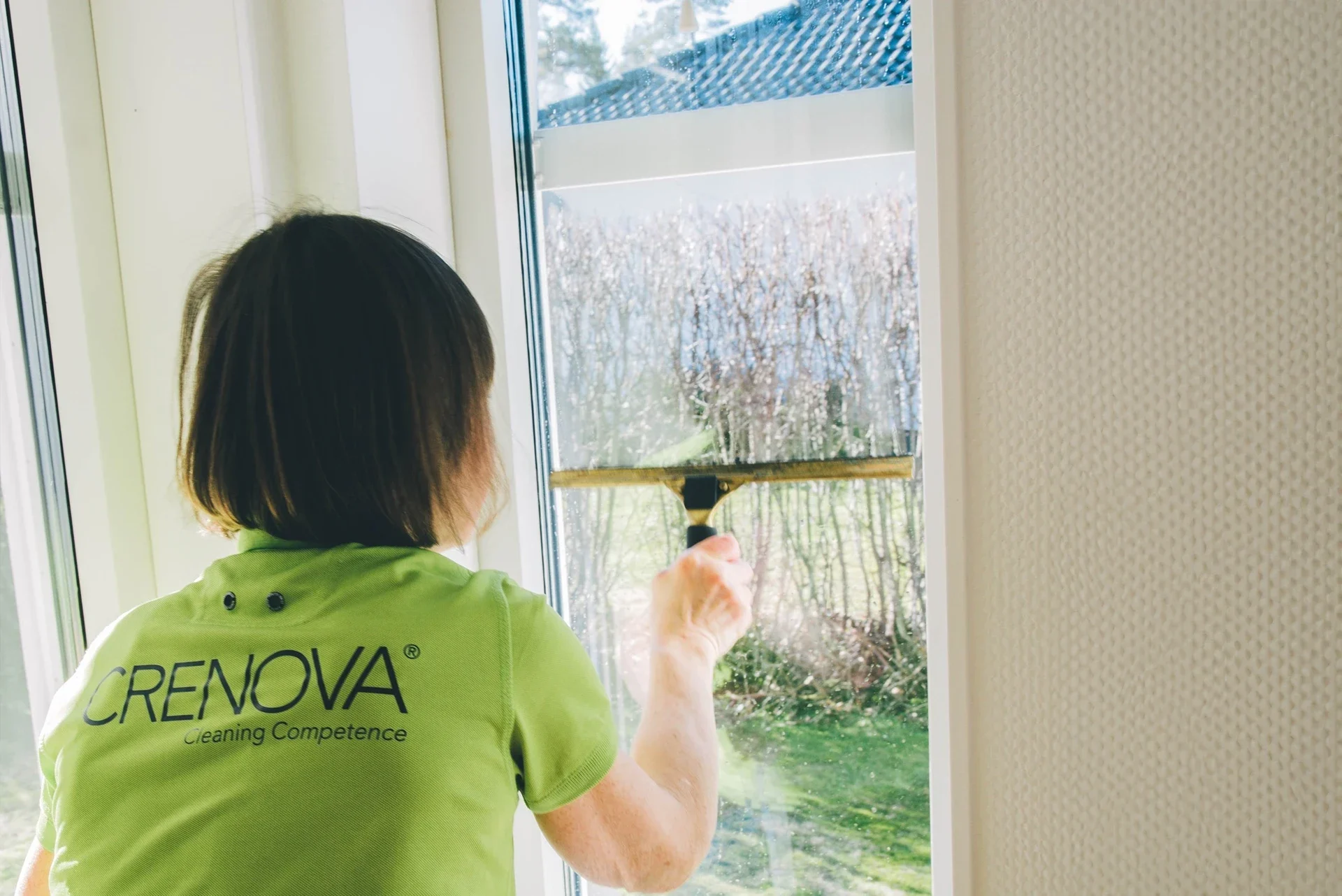 Fönsterputsare med grönt tröja rengör ett fönster.
